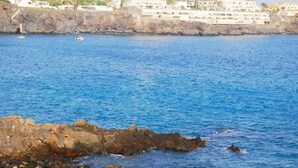Une zone côtière caractérisée par un littoral rocheux, une eau d’un bleu limpide et des bâtiments visibles à l’arrière-plan.