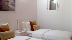 Une chambre d’hôtel avec deux lits, chacun étant équipé de draps blancs et d’oreillers marron. On y trouve une petite table de chevet avec une lampe et un miroir.