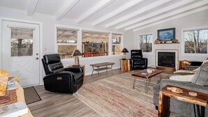 A modern living room with a fireplace, leather chairs, a sofa, and large windows offering a view of the outdoors. - Private Home on the Kenai River at Gull's Landing (Soldotna)