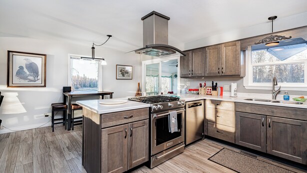 A modern kitchen with wooden cabinets, stainless steel appliances, and a large window providing natural light. - Private Home on the Kenai River at Gull's Landing (Soldotna)