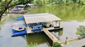 A docked boat house with a covered deck, surrounded by calm water and greenery.