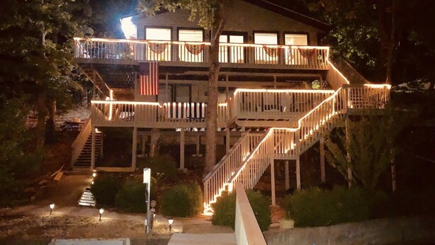 A waterfront property with a wooden deck, multiple balconies, and a staircase leading to the upper levels.