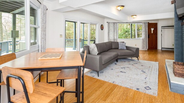 Een ruime woonkamer met een houten eettafel, een grijze bank en een groot raam met uitzicht op de omgeving.