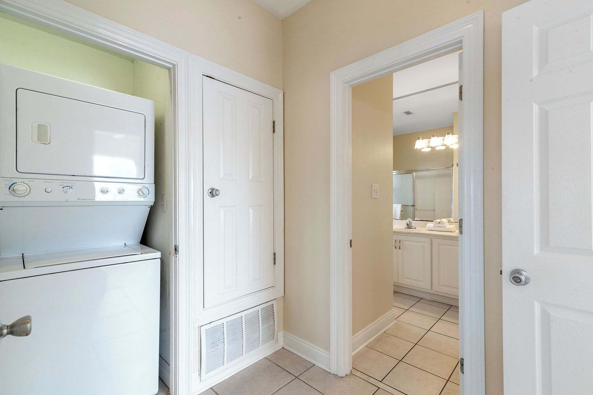 A laundry room with stacked washers and dryers, a door leading to a bathroom with a sink and mirror.
