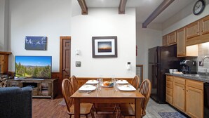 A dining area with a wooden table set for four, surrounded by wooden chairs. A television is mounted on the wall to the left. - Whistlepunk 36: 1 Br Plus Bonus Sleeping Loft Slope Side (Snowshoe)