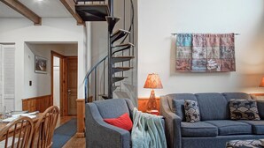 A living room with a staircase, a dining area with wooden furniture, and a patterned wall hanging. - Whistlepunk 36: 1 Br Plus Bonus Sleeping Loft Slope Side (Snowshoe)