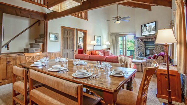 A spacious dining area with a wooden table set for four, a staircase, and a cozy living room with a fireplace. - Whistlepunk 13 Spacious 4 Br Condo Slope Side (Snowshoe)