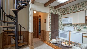 A kitchen with a wooden staircase, a microwave, a stove, and a dining table set with plates and glasses.