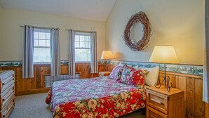 A bedroom with a bed, two bedside tables, a wall-mounted lamp, and a window with curtains.