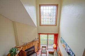 A high-ceilinged room with a fireplace, a window with a view of the outdoors, and a balcony with a railing. - Whistlepunk 40 Bavaria`s Finest-1 bedroom with loft, Slope Side (Snowshoe)