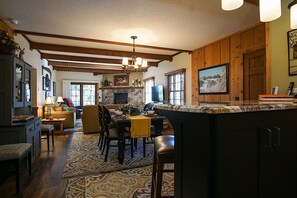 A spacious kitchen with a stone fireplace, wooden beams, and a large island with bar stools.