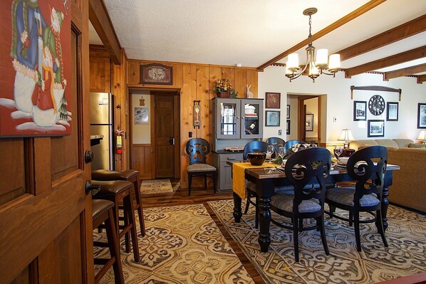 A cozy dining area with a wooden table and chairs, a chandelier, and a patterned rug.