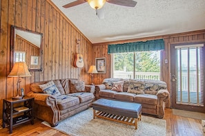 A cozy living room with wooden walls, two sofas, a coffee table, and a ceiling fan.