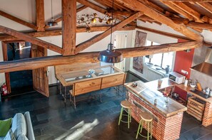 A rustic kitchen with exposed wooden beams, a central island with stools, and a hanging light fixture.