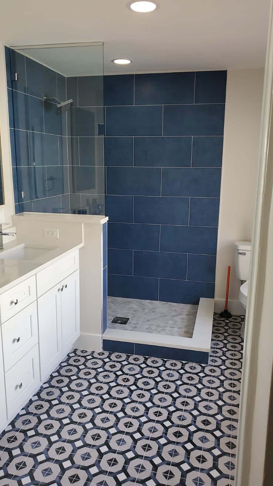 A bathroom with a white vanity, a large mirror, dark blue tiled walls, and a patterned floor.