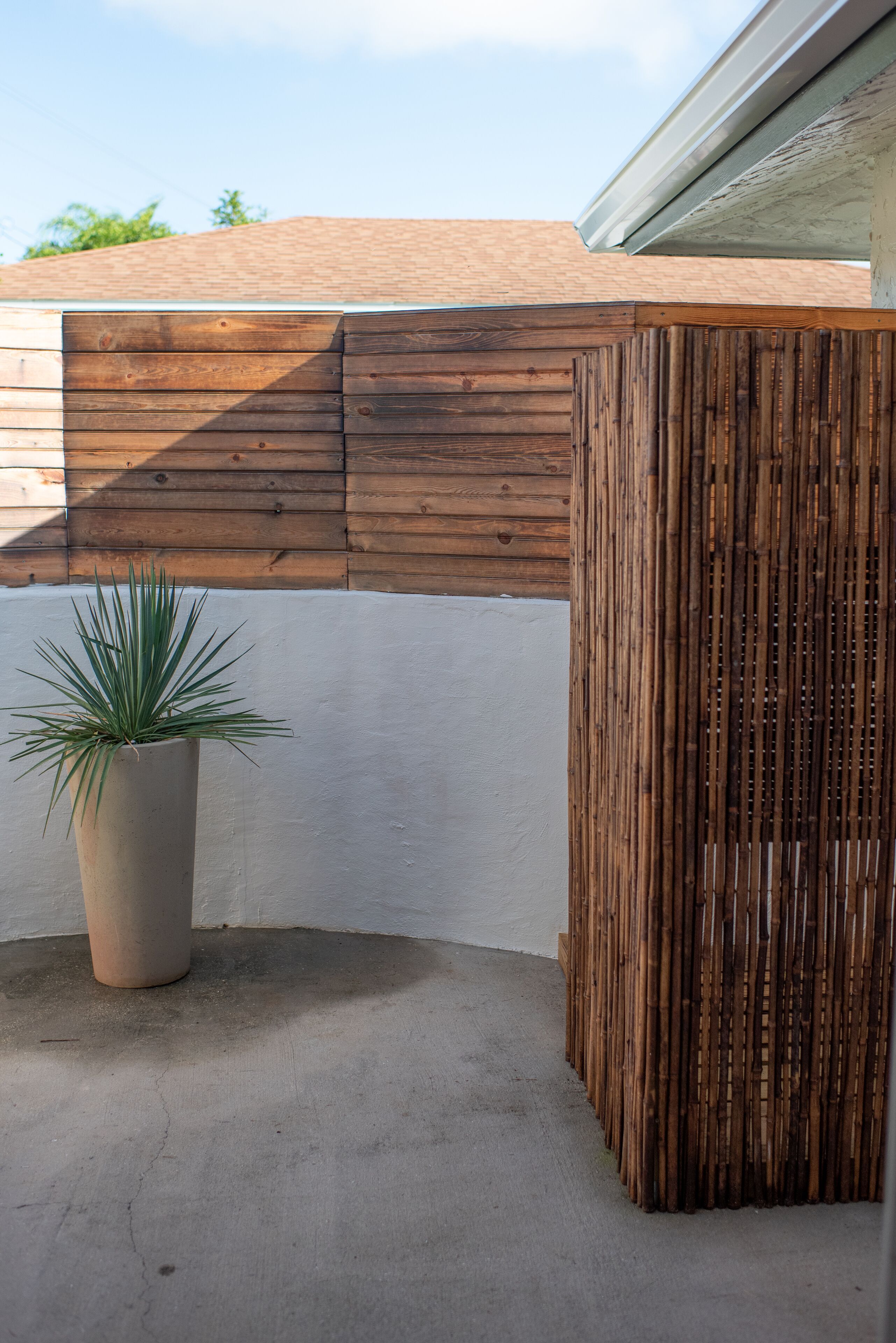 Esquina de un edificio con valla de madera, suelo de hormigón y planta en maceta.