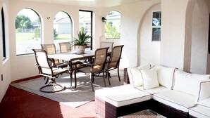 Ein sonnendurchflutetes Zimmer mit Esstisch, Stühlen, einer Couch und Bogenfenstern.