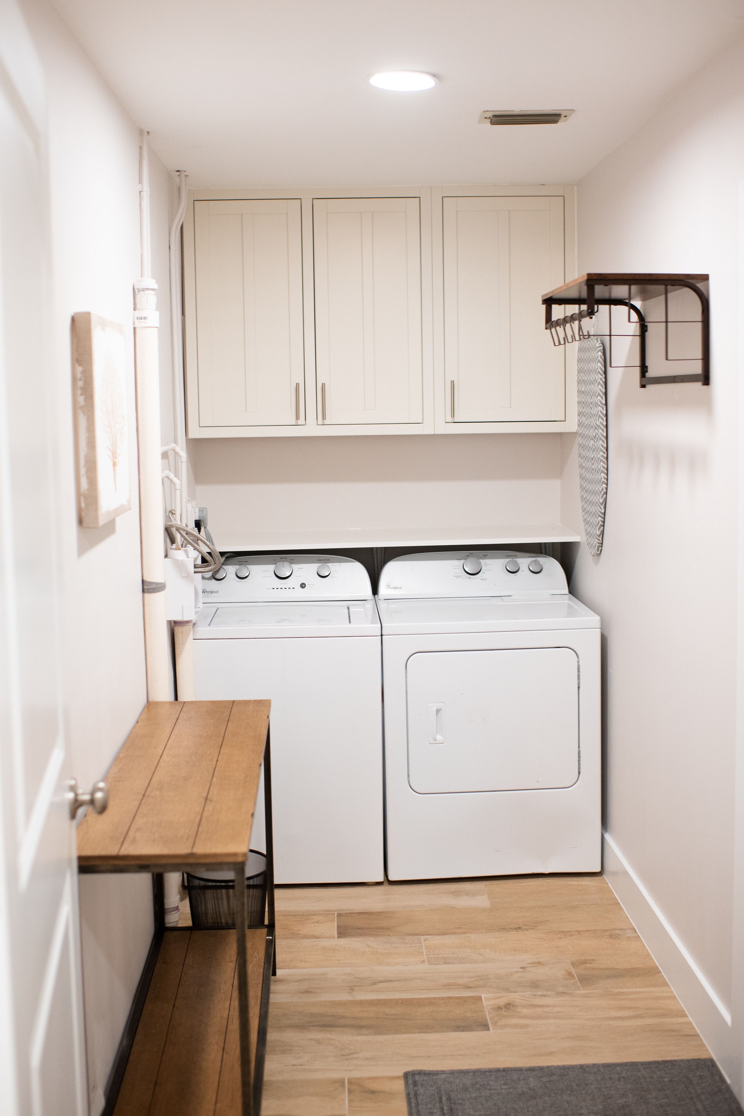 A compact laundry room with a washing machine and dryer, a small wooden table, and a towel rack.