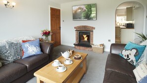 A cozy living room with a fireplace, a sofa, a coffee table, and a kitchen visible through an archway. - Two bedroomed property situation in a beautiful secluded location with patio area overlooking fields (Wootton Wawen)