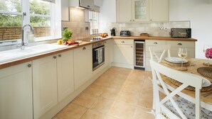 A kitchen with white cabinets, a tiled floor, a sink, a stove, and a dining area with a table and chairs. - Two bedroomed property situation in a beautiful secluded location with patio area overlooking fields (Wootton Wawen)