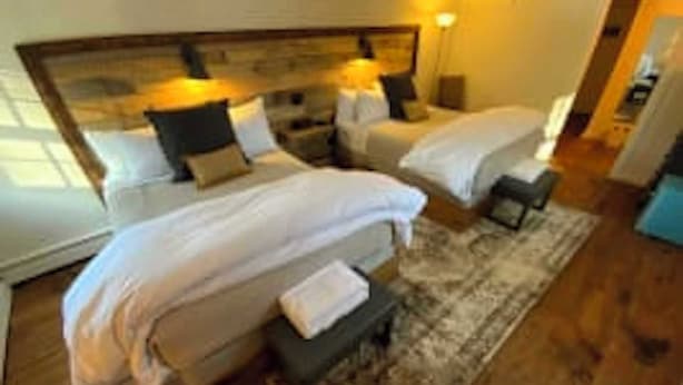 Habitació d'hotel amb dos llits individuals, un capçal de llit de fusta, una petita taula de nit i una tauleta amb una làmpada.