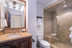 Une salle de bain équipée d’un lavabo, d’un miroir et d’une douche séparée par des parois en verre.
