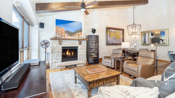 A spacious living room with a fireplace, leather seating, a large flat-screen TV, and a ceiling fan.
