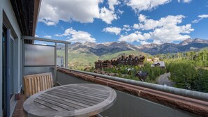 A balcony with a wooden table and chairs, overlooking a mountainous landscape with buildings.