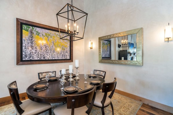 Un coin repas avec une table ronde dressée pour six personnes, entourée de chaises, d’un lustre et d’œuvres d’art murales.