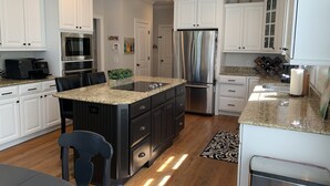 A modern kitchen with white cabinetry, stainless steel appliances, a granite countertop, and a central island with bar stools. - LUXURY HOME INCLUDES GOLF CART walking distance to historic village center (Pinehurst)