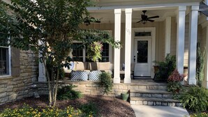 A house with a stone facade, a covered porch with columns, a front door, and a small garden with yellow flowers. - LUXURY HOME INCLUDES GOLF CART walking distance to historic village center (Pinehurst)