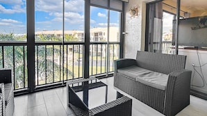 Ein Balkon mit einer Rattan-Couch, einem kleinen Tisch und Blick auf eine Wohngegend.