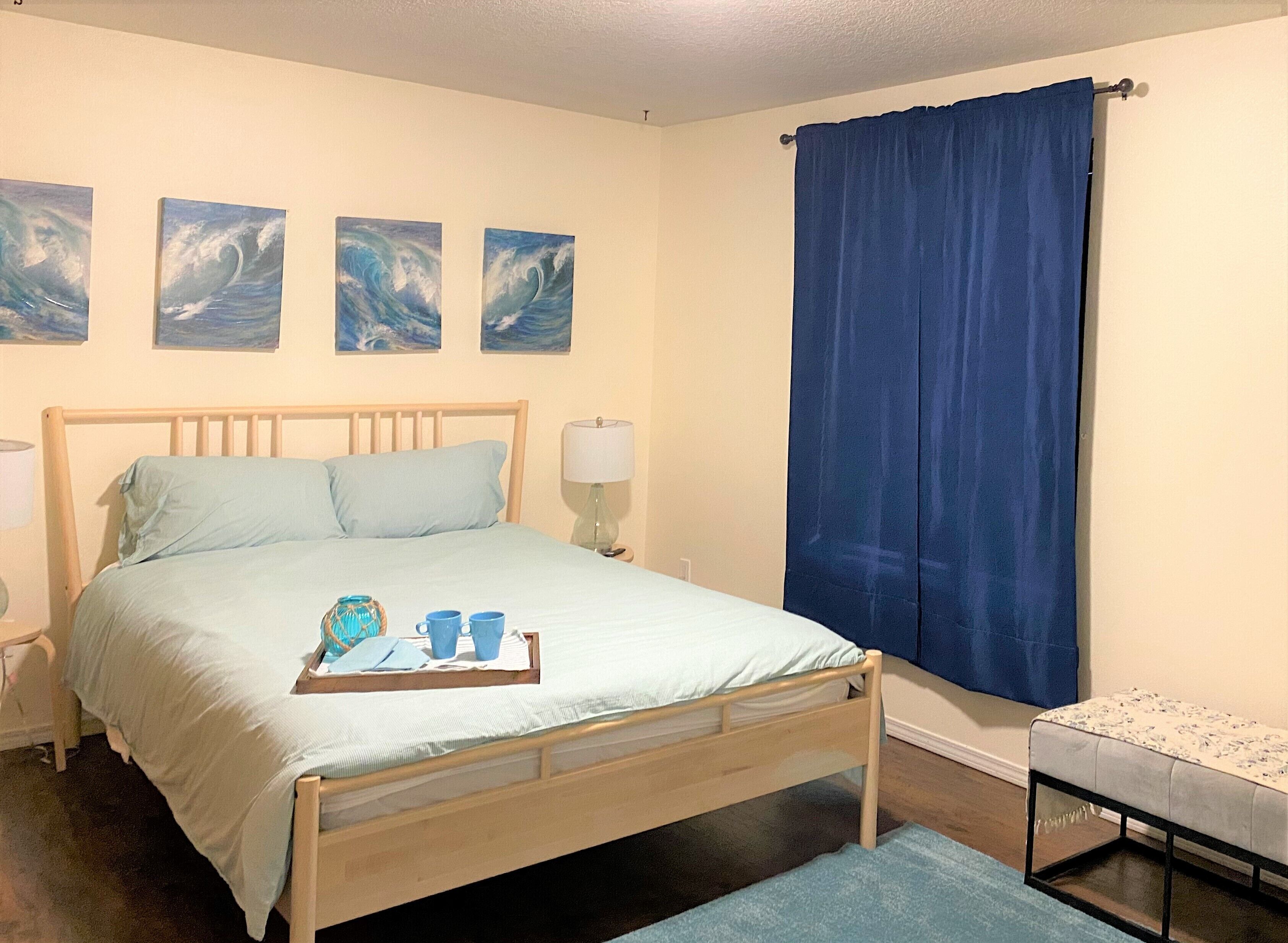 A bedroom with a wooden bed, a bedside table with a lamp, and three paintings on the wall.