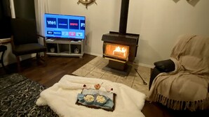 A living room with a television displaying various channels, a fireplace, a cozy seating area, and a decorative wall piece. - Breathtaking ocean views & adventure at your doorstep (Newport)
