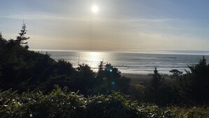 A coastal view with the sun reflecting off the water, surrounded by dense foliage and a clear sky. - Breathtaking ocean views & adventure at your doorstep (Newport)