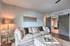 A modern living room with a sectional sofa, a coffee table with decorative items, a lamp, and a wall-mounted artwork.