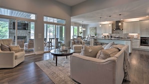 Amplia sala de estar con chimenea, comedor y cocina con gabinetes blancos y salpicadero de piedra.