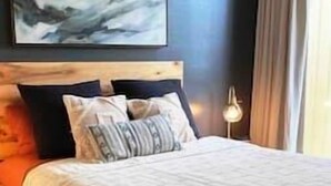 A neatly made bed with a striped pillow and a headboard against a dark wall. - Hidden Gem! Turtle Bay Hideaway (Kahuku)
