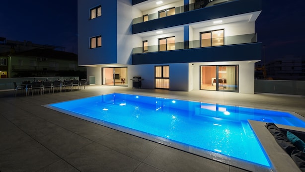A modern building with a swimming pool, outdoor seating, and multiple balconies.