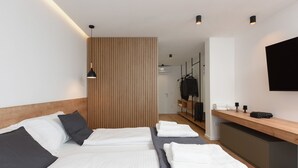 A hotel room with two beds, a wooden headboard, a flat-screen TV, a wooden desk, and a wardrobe.