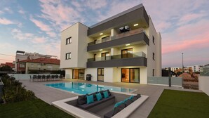 A modern multi-story building with a swimming pool and outdoor seating area.