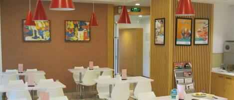 Un comedor con mesas y sillas, lámparas colgantes rojas y decoración en la pared.