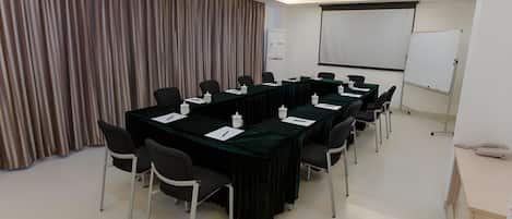 Une salle de conférence équipée d’une longue table, de chaises, d’un projecteur et d’un tableau blanc.