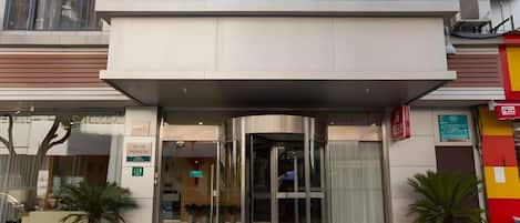 Entrada de hotel com design moderno, com porta de vidro e área de acesso coberta.