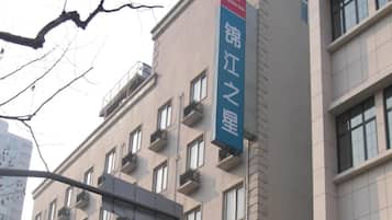 Un edificio con múltiples ventanas y balcones, un letrero de Jinjiang Inn, y un cielo despejado.