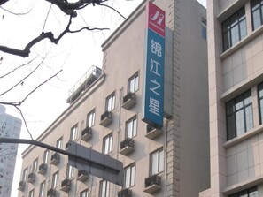 En byggnad med många fönster och balkonger, en skylt för Jinjiang Inn och en klar himmel.