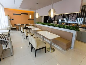 A modern restaurant interior with white tables and benches, pendant lighting, and a counter with a green plant display. - Jinjiang Inn (Shanghai Changzhong Road Subway Station) (Shanghai)