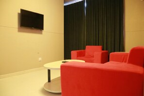 A room with a flat-screen TV mounted on the wall, a round table, and two red chairs. - Jinjiang Inn (Shanghai Changzhong Road Subway Station) (Shanghai)