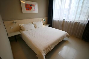 A hotel room with a large bed, a bedside table with a lamp, a painting on the wall, and a window with curtains. - Jinjiang Inn (Shanghai Changzhong Road Subway Station) (Shanghai)
