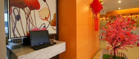 A reception desk with a laptop, a framed abstract artwork, and a decorative pink tree in a lobby.